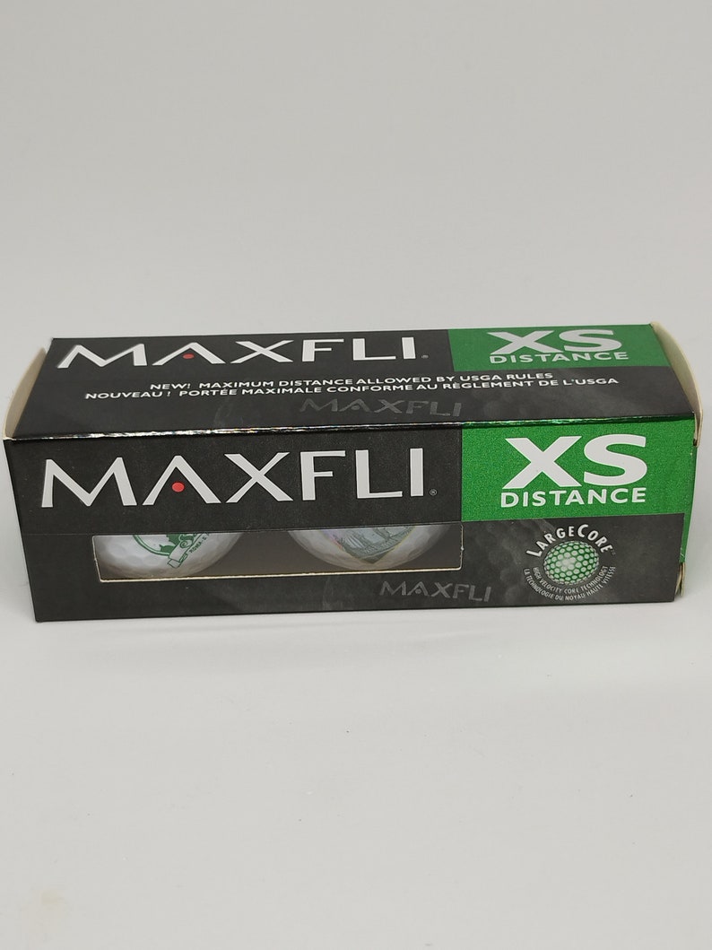 May include: A package of three Maxfli XS Distance golf balls. The package is black with green and white text. The golf balls are white with green and white markings.