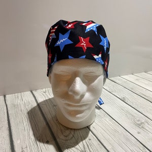 May include: A black surgical scrub cap featuring a pattern of red, white, and blue stars, with medical symbols. The cap is designed to be worn in a medical setting.