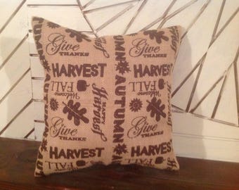 May include: A brown burlap pillow with the words "Give Thanks", "Harvest", "Fall", and "Autumn" printed on it in a dark brown color.