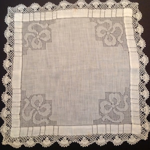 May include: A white linen handkerchief with a delicate crocheted border and floral designs in the corners.