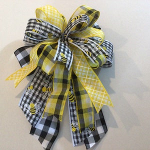 May include: A yellow and black checkered ribbon bow with a yellow ribbon with a white and yellow checkered pattern and a yellow ribbon with a bee print.