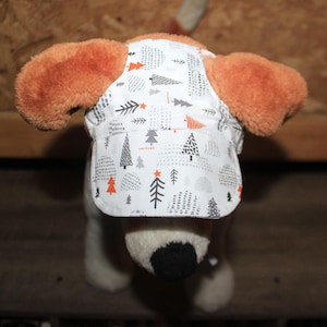 May include: A white dog hat featuring a pattern of black, grey, and orange trees and stars. The hat is worn by a dog with brown ears. The hat is designed to shield the dog's eyes from the sun.