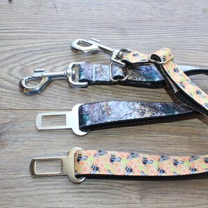 May include: A camouflage and bee-patterned dog seatbelt tether with two metal clips and a safety buckle.