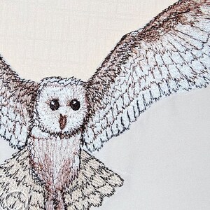 May include: A white and brown embroidered barn owl with its wings spread out. The owl is facing the camera with its eyes open.