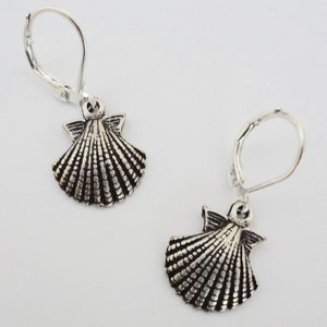 May include: A pair of silver earrings featuring a scallop shell design. The earrings have a leverback fastening.