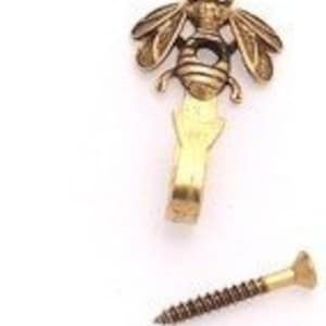 May include: A gold-toned metal bee hook with a screw for hanging. The bee is detailed with wings, legs, and a stinger.