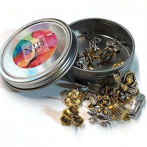 May include: A silver metal container with a lid, featuring a colorful watercolor design on the lid. The container is filled with a variety of small, decorative metal pins, including butterflies, bees, and other nature-inspired designs.