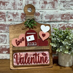 May include: Wooden Valentine's Day sign with a red mailbox, hearts, and the words "love", "XOXO", "cutie", and "Valentine".