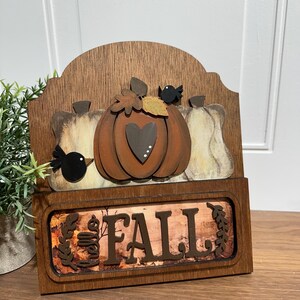 May include: Wooden sign with a fall theme. It features a pumpkin with a heart, two birds, and the words "Hello Fall".