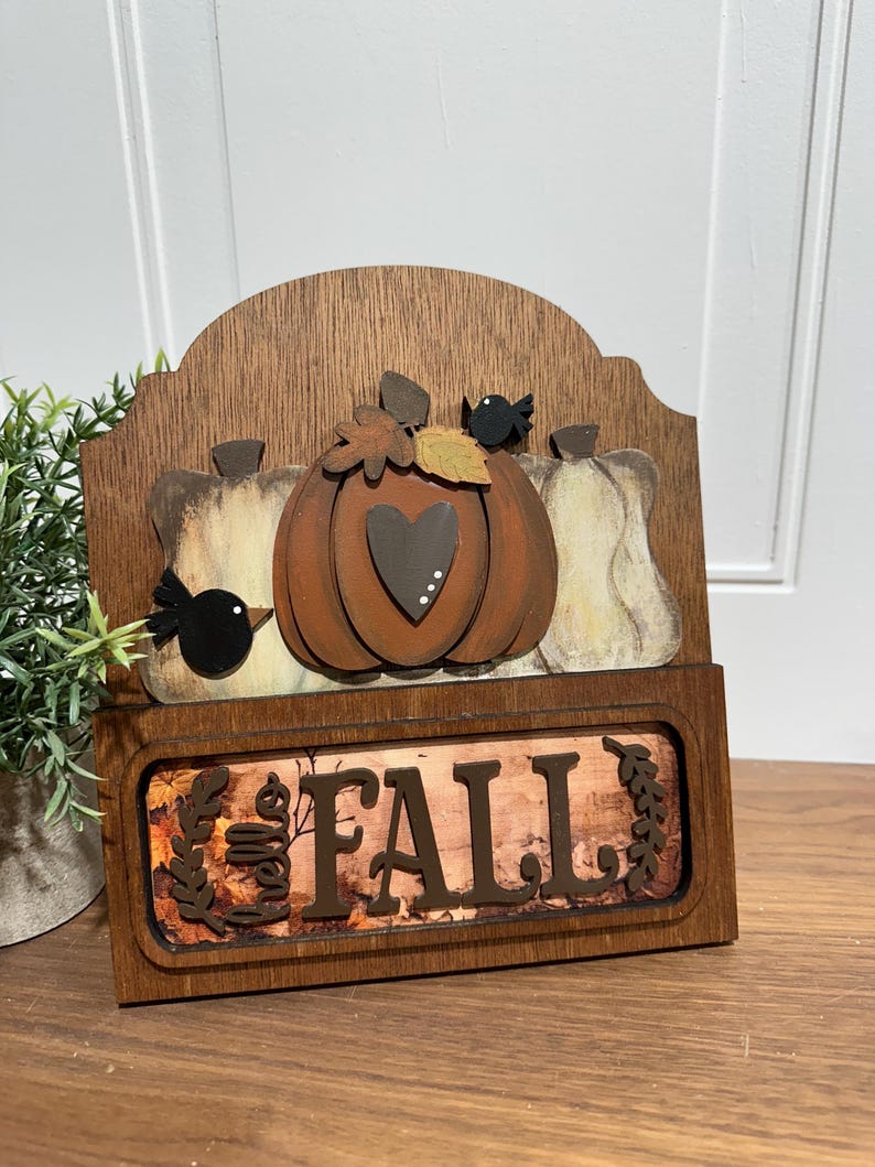 May include: Wooden sign with a fall theme. It features a pumpkin with a heart, two birds, and the words "Hello Fall".