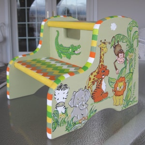 May include: A green and yellow painted wooden step stool with a jungle animal theme. The stool features a giraffe, lion, zebra, elephant, monkey, and alligator. The top of the stool has a yellow handrail.