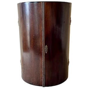 May include: A dark brown wooden cabinet with a rounded front and two doors. The cabinet has brass hardware and is closed.