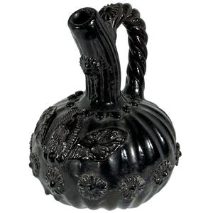 May include: A black glass pitcher with a round body and a twisted handle. The pitcher features embossed floral and leaf designs, along with a spout and a series of small, raised dots. The overall design is ornate and decorative.