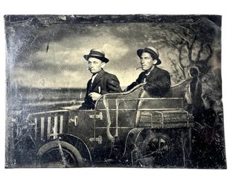 May include: A black and white tintype photograph of two men in straw hats sitting in a horse-drawn carriage. The men are dressed in suits and ties. The carriage is decorated with wicker.