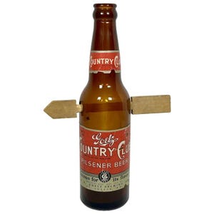 May include: A brown glass beer bottle with a red and white label that reads "Goetz Country Club Pilsener Beer." Two wooden arrow-shaped pieces are attached to the bottle. The bottle is a vintage item.