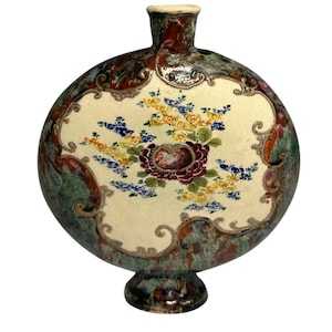May include: A round, ceramic vase with a wide base and a narrow neck. The vase is decorated with a floral pattern in shades of red, yellow, blue, and green. The vase has a mottled, textured surface.