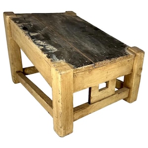 May include: A small wooden stool with a rectangular top and four sturdy legs. The top surface is dark brown with visible wood grain, while the frame and legs are finished in a distressed, light cream-colored paint showing signs of wear.