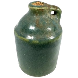 May include: A small green ceramic jug with a cork stopper and a handle. The jug has a rustic, handmade look.