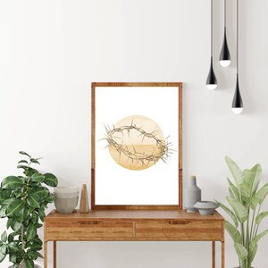 May include: A framed print of a watercolor illustration of a crown of thorns on a yellow circle. The print is hanging on a white wall above a wooden table.