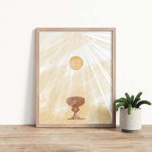 May include: A framed print with a minimalist design featuring a golden chalice and host with a cross on a light beige background with white rays of light.