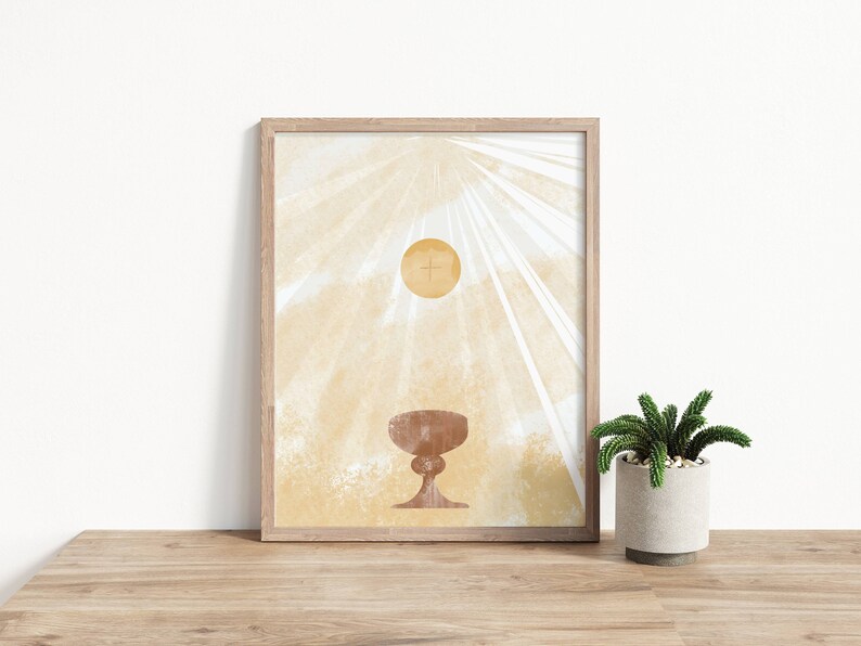 May include: A framed print with a minimalist design featuring a golden chalice and host with a cross on a light beige background with white rays of light.
