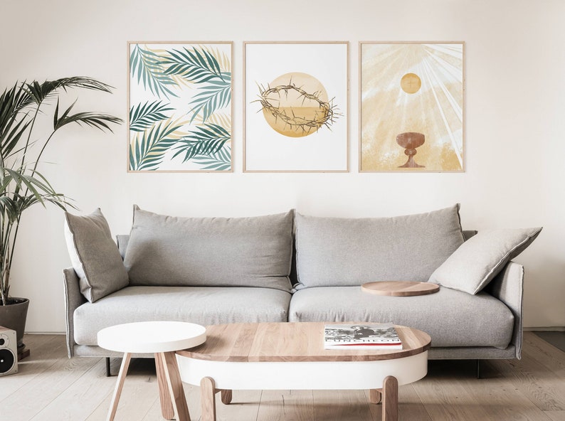 May include: Three minimalist art prints with religious imagery. The prints feature a palm leaf design, a crown of thorns, and a chalice with a sunburst behind it. The prints are displayed on a white wall above a gray sofa.