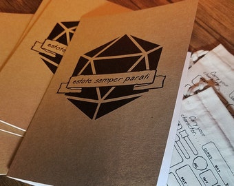 May include: Three brown notebooks with a black and white illustration of a twenty-sided die and the text "estote semper parati".