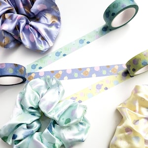 May include: Four colorful patterned scrunchies with pastel colors and geometric shapes. The scrunchies are made of satin fabric and are perfect for adding a touch of style to any outfit.