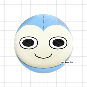 May include: A circular pinback button featuring a light blue background and a central cream-colored face with large black oval eyes and a simple black curved mouth. The text "pecknorder" is printed in small black letters near the bottom right edge.