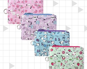 May include: Four colorful zippered wallets with different patterns. Each wallet has a small ring attached to the side. The patterns include pink with cherries and hearts, purple with skulls and stars, blue with lips and crowns, and green with strawberries and smiley faces.