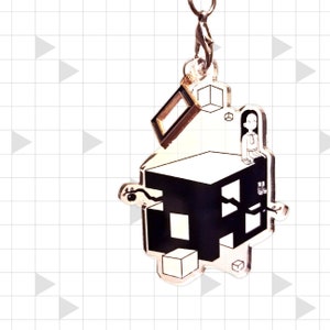 Puede incluir: Un llavero de acrílico transparente con un diseño geométrico en blanco y negro y una pequeña figura sentada. El llavero tiene un cierre y un anillo plateados. El diseño incluye formas de cubo y una ilustración estilizada.