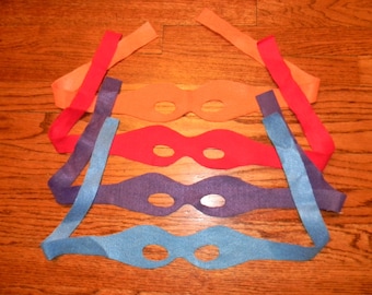 May include: Five felt eye masks in different colors, orange, red, purple, blue, and light blue, with elastic straps. The masks are arranged in a stack, with the orange mask on top and the light blue mask on the bottom.