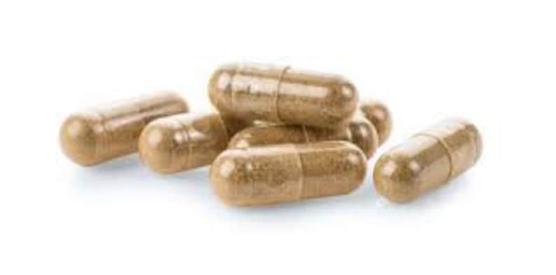 May include: A close-up of a pile of brown capsules on a white background. The capsules are made of a clear material and contain a brown powder.
