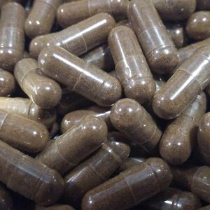 May include: A close-up image of a large pile of brown capsules. The capsules are made of clear plastic and contain a brown powder.