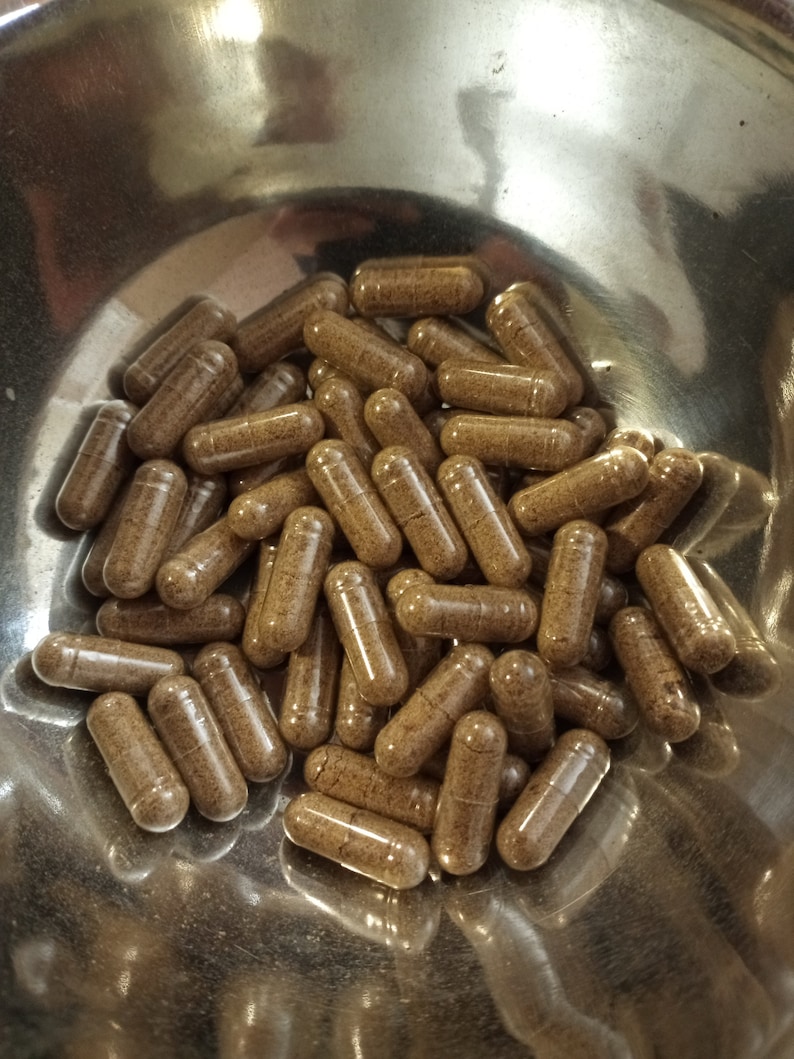 May include: A collection of brown capsules fills a shiny, metallic bowl. The capsules are cylindrical with rounded ends, and appear to be filled with a granular substance. The lighting creates highlights and shadows on the capsules and bowl.