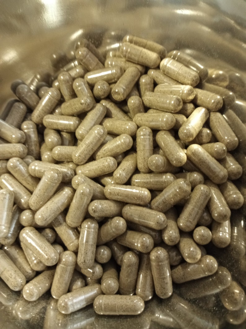May include: A close-up view of a large quantity of brown capsules in a silver bowl. The capsules are filled with a light brown powder.