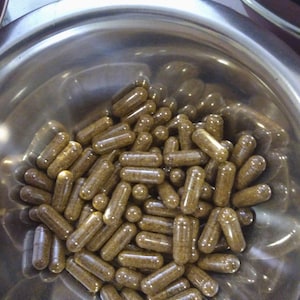 May include: A metal bowl filled with a large quantity of brown capsules. The capsules are translucent and filled with a brown powder.