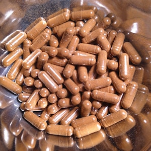 May include: A bowl filled with a large quantity of brown capsules. The capsules are transparent and show the brown powder inside.