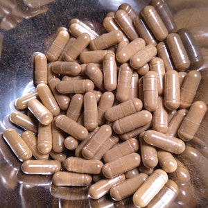 May include: A bowl filled with brown capsules. The capsules are made of a clear material and contain a brown powder.
