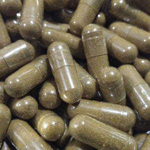 May include: A close-up shot of numerous brown capsules, likely supplements or medications. The capsules are filled with a light brown powder and are arranged in a random, overlapping pattern. The capsules have a smooth, glossy appearance.