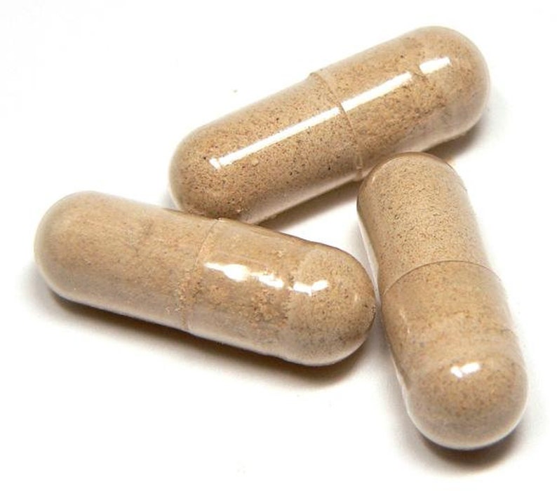 May include: Three beige capsules with a light brown powder inside are arranged on a white background. The capsules are cylindrical with rounded ends and a clear, glossy exterior. The capsules are slightly translucent, revealing the powder within.