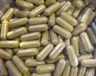 May include: A close-up shot of numerous olive-green capsules. The capsules are filled with a green powder and are scattered in a stainless steel bowl. The capsules are cylindrical with rounded ends.