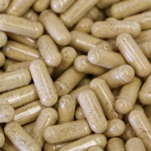 May include: A close-up image of a large pile of beige capsules. The capsules are translucent and filled with a light brown powder.