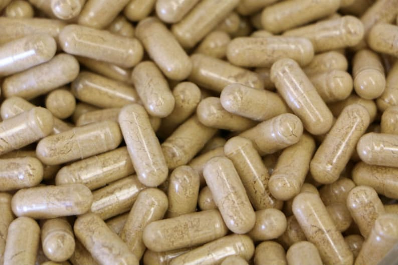 Pu&ograve; includere: Un'immagine ravvicinata di un grande mucchio di capsule beige. Le capsule sono traslucide e riempite con una polvere marrone chiaro.