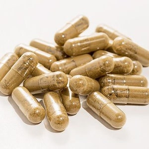 May include: A pile of brown capsules on a white surface. The capsules are all the same size and shape, and they are arranged in a random pattern.