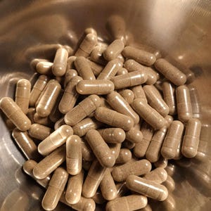 May include: A bowl filled with a large quantity of brown capsules. The capsules are translucent and show a brown powder inside.
