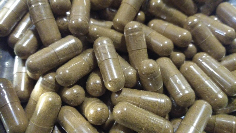Pu&ograve; includere: Un'immagine ravvicinata di un grande mucchio di capsule trasparenti riempite con una polvere marrone. Le capsule sono disposte in uno schema casuale.
