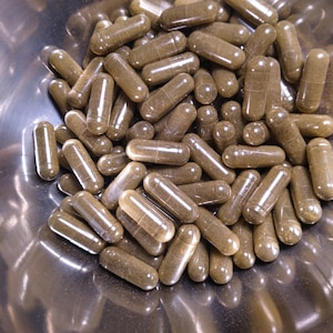 May include: A metal bowl filled with a large quantity of brown capsules. The capsules are translucent and filled with a brown powder.