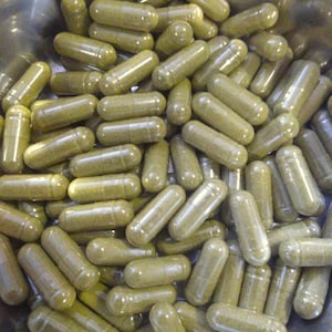 May include: A close-up view of a bowl filled with many green capsules. The capsules are made of clear plastic and contain a green powder.