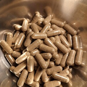 May include: A bowl filled with a large quantity of brown capsules. The capsules are translucent and show a brown powder inside.